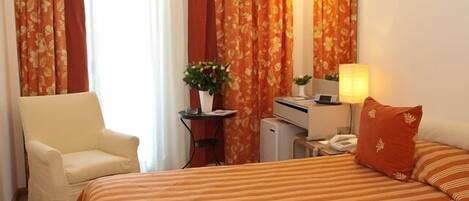 A hotel room with a bed, a chair, a desk with a computer, a lamp, and a mirror.