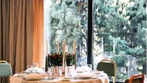 A dining area with a round table set for four, large windows with a view of trees, and a curtain on the left. - The Park Hotel Piraeus (Piraeus)