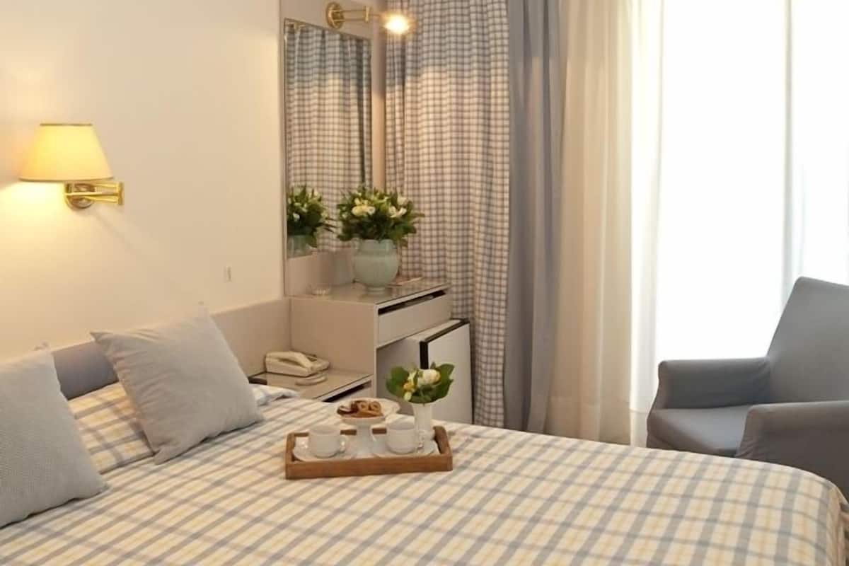 A hotel room with a bed, a desk, a chair, and a window with curtains.