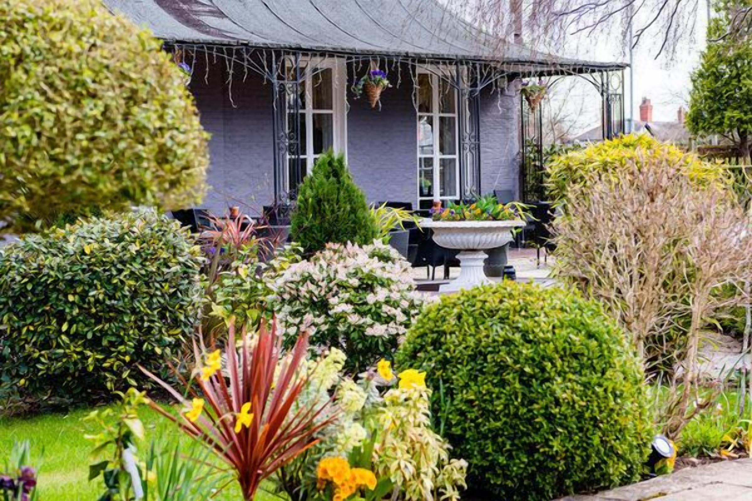 Un jardín con diversas plantas y un edificio con porche cubierto.