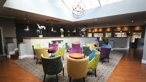 A spacious indoor area with a high ceiling, a central bar area, and multiple colorful chairs arranged around tables. - Rossett Hall Hotel (Wrexham)