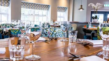 A dining area with tables set for a meal, featuring patterned tablecloths and clear glassware.