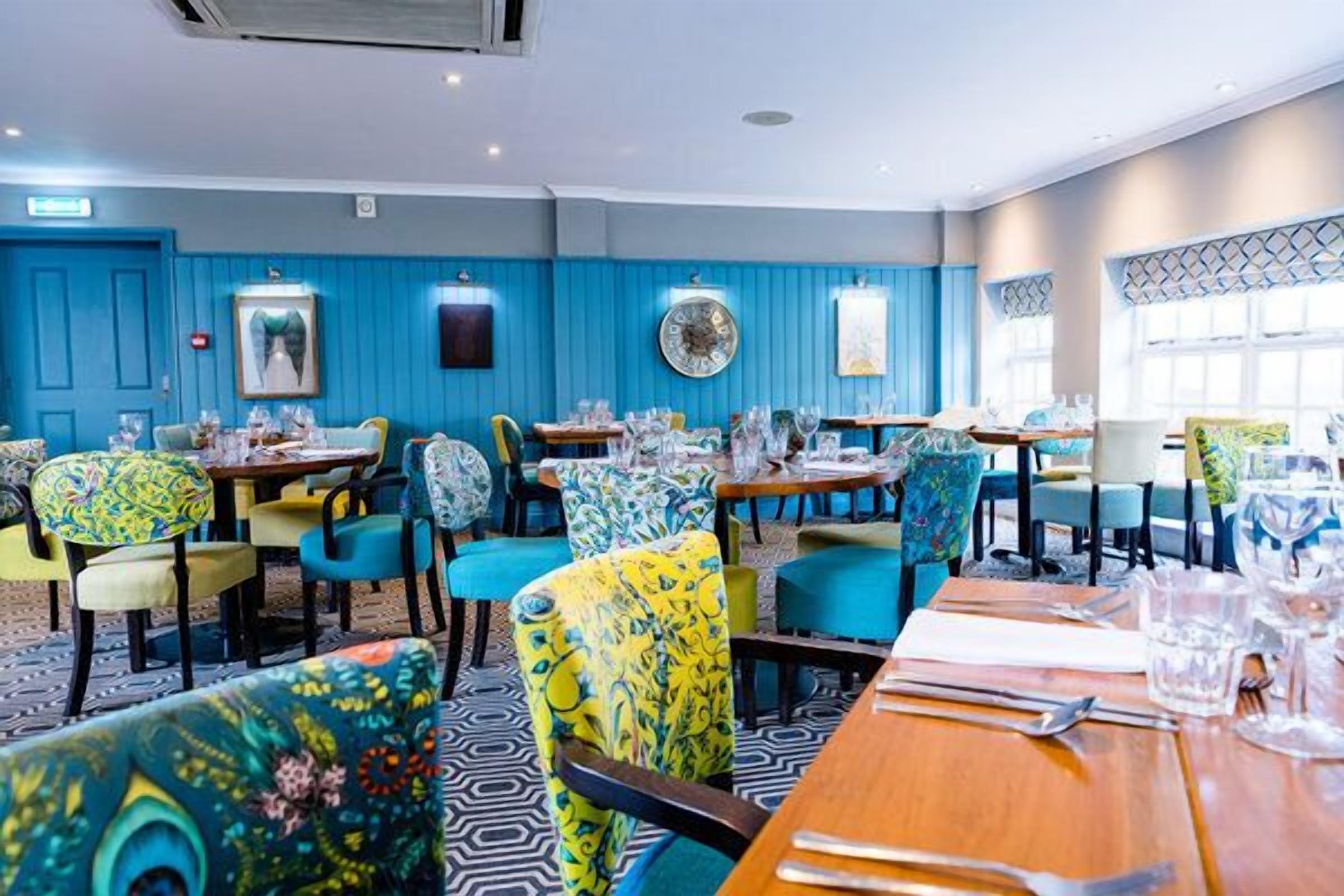 A restaurant with blue walls, colorful patterned chairs, and tables set for dining.
