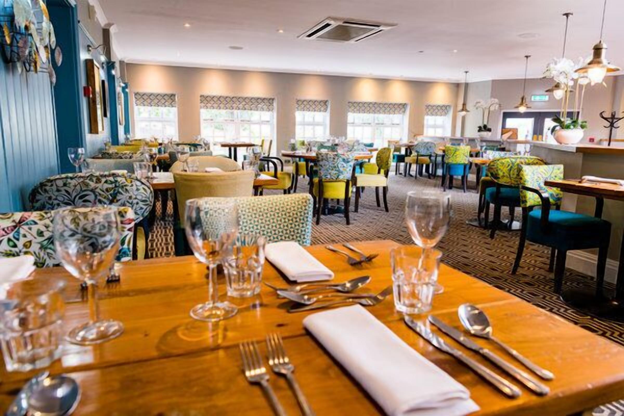 A restaurant with multiple tables, each set with cutlery and glasses.