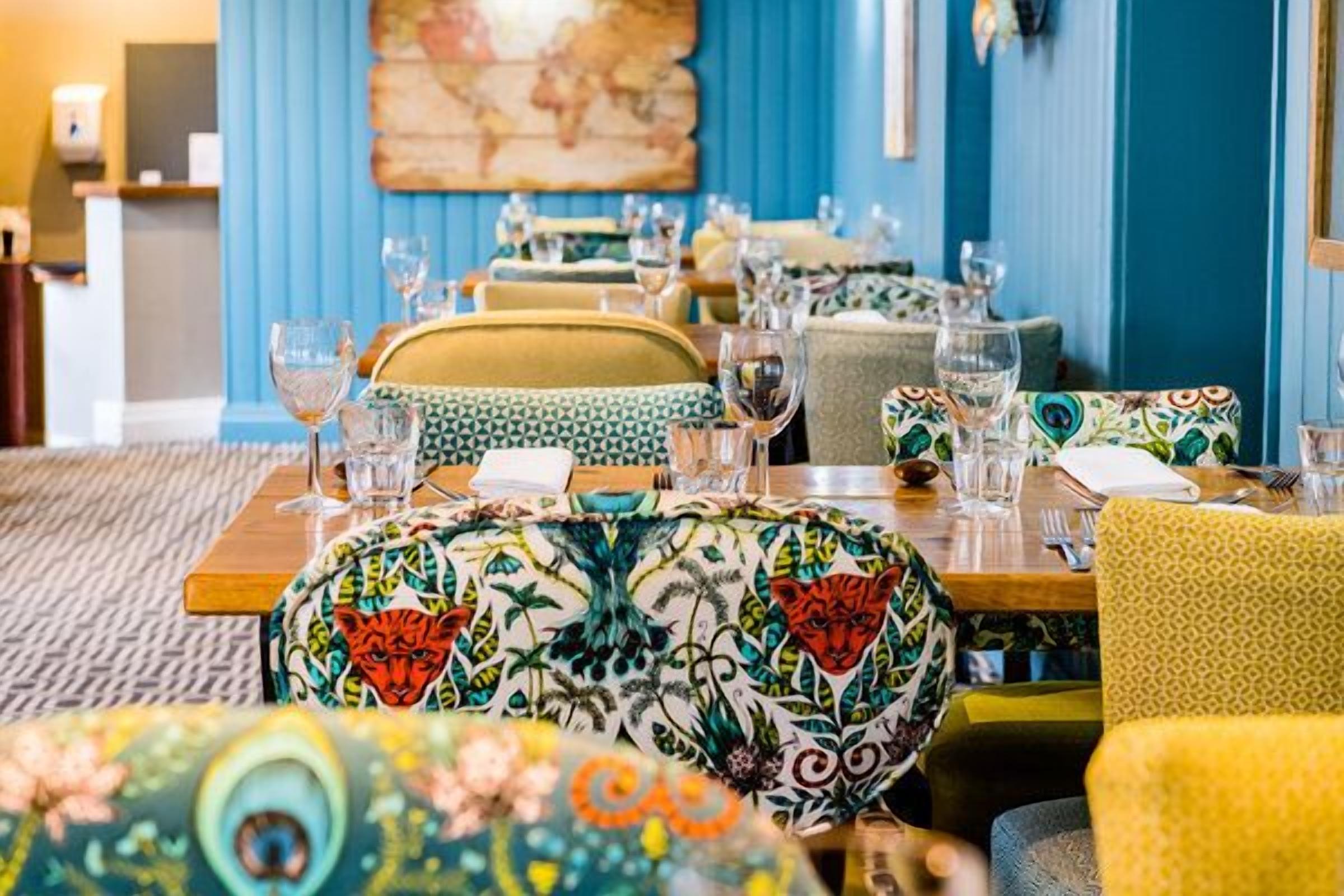 A dining area with tables set for service, featuring patterned tablecloths and chairs.