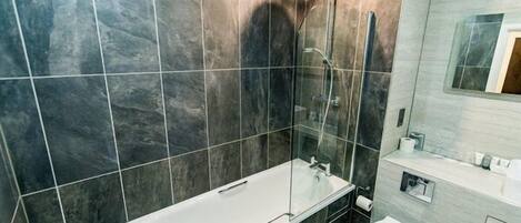 Moderni kylpyhuone, jossa on lasiseinällä varustettu suihku, valkoinen kylpyamme ja wc.