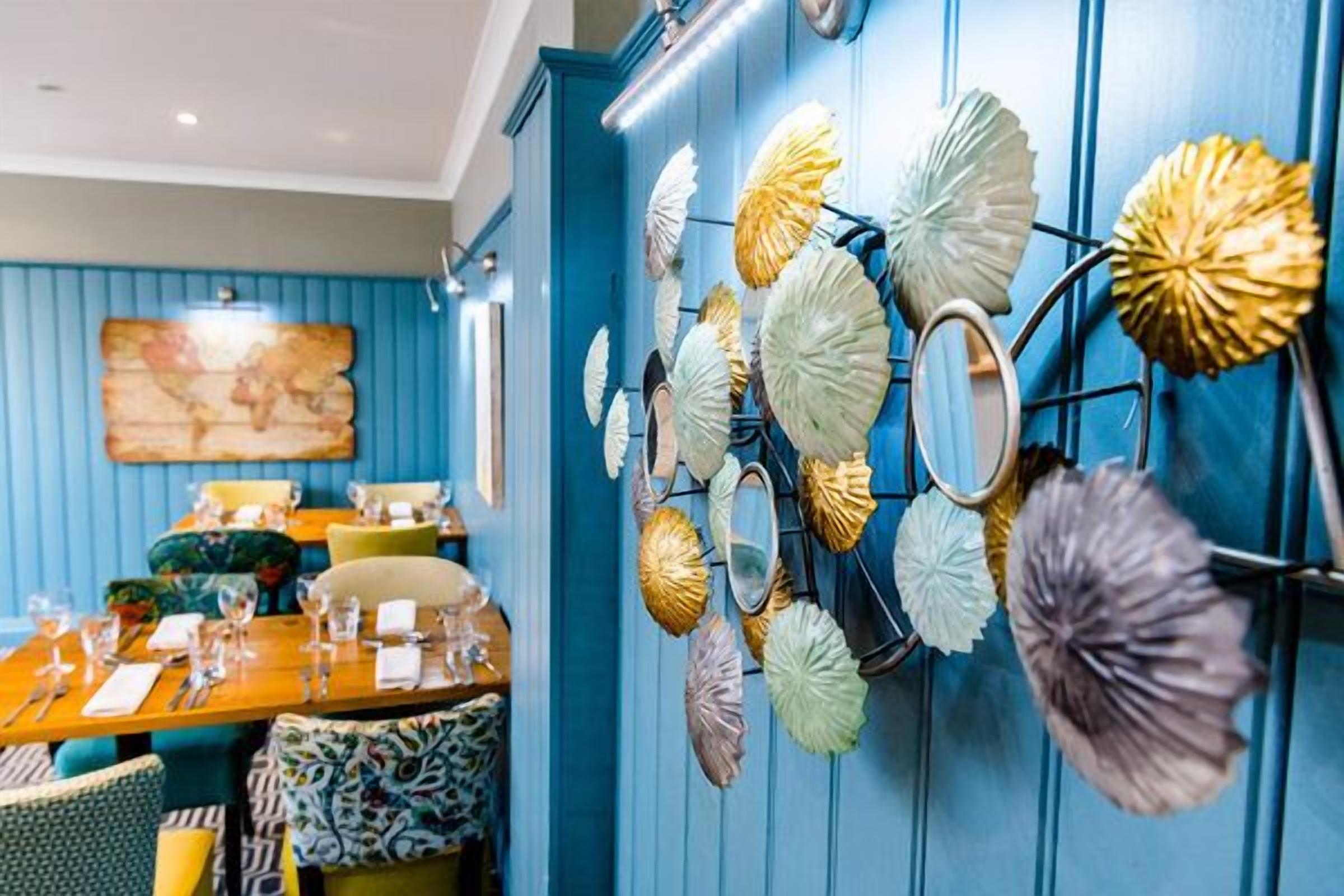 Een restaurantinterieur met blauwe wanden, een wereldkaart als kunstwerk en een wanddecoratie van bladeren.