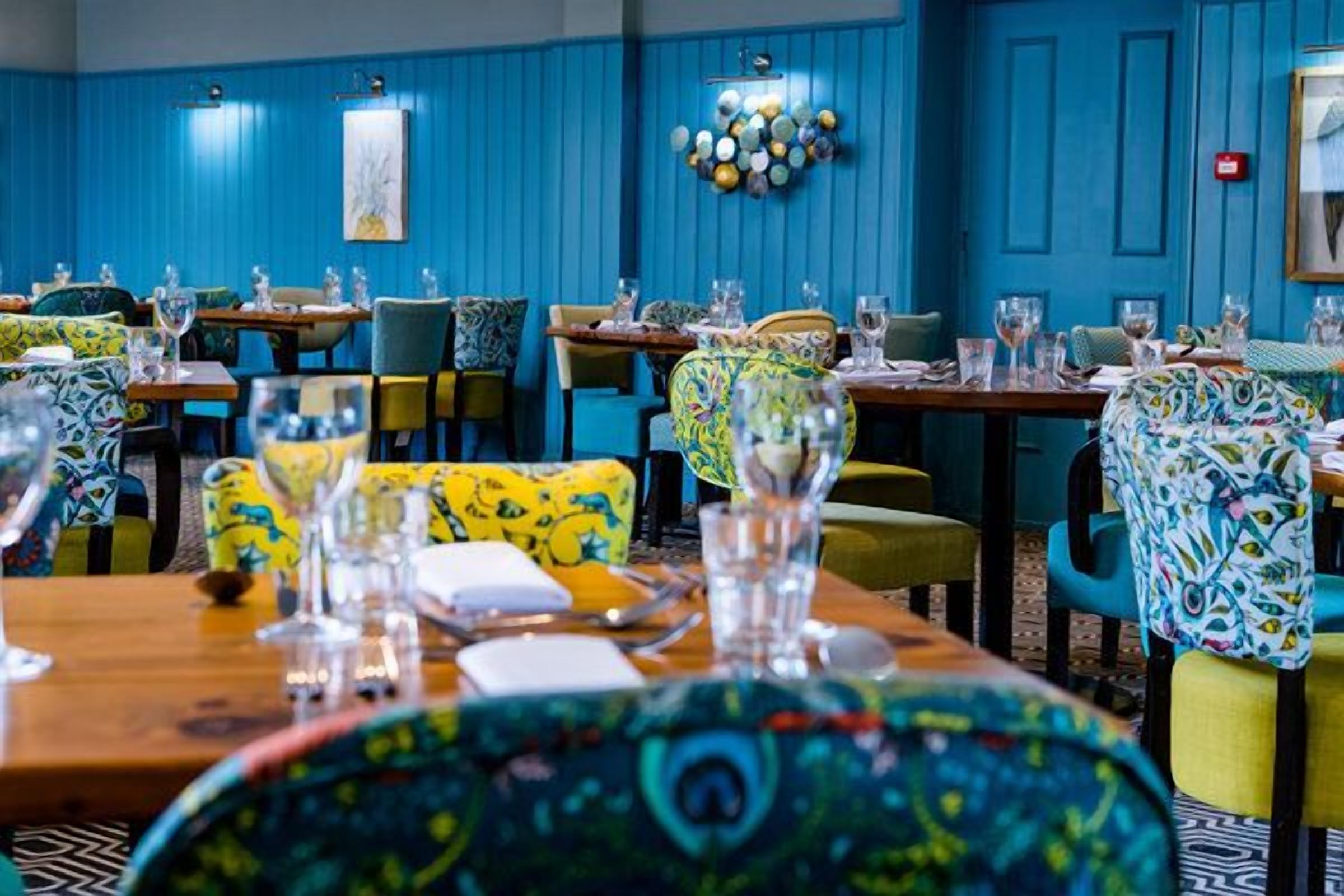 A restaurant with blue walls, colorful chairs, and tables set for dining.