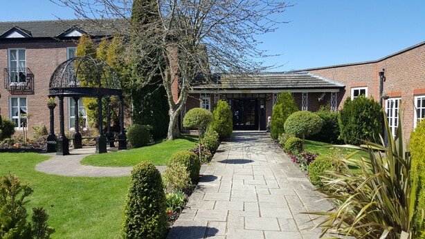 A brick building with a paved pathway, a gazebo, and well-maintained hedges. - Rossett Hall Hotel (Wrexham)