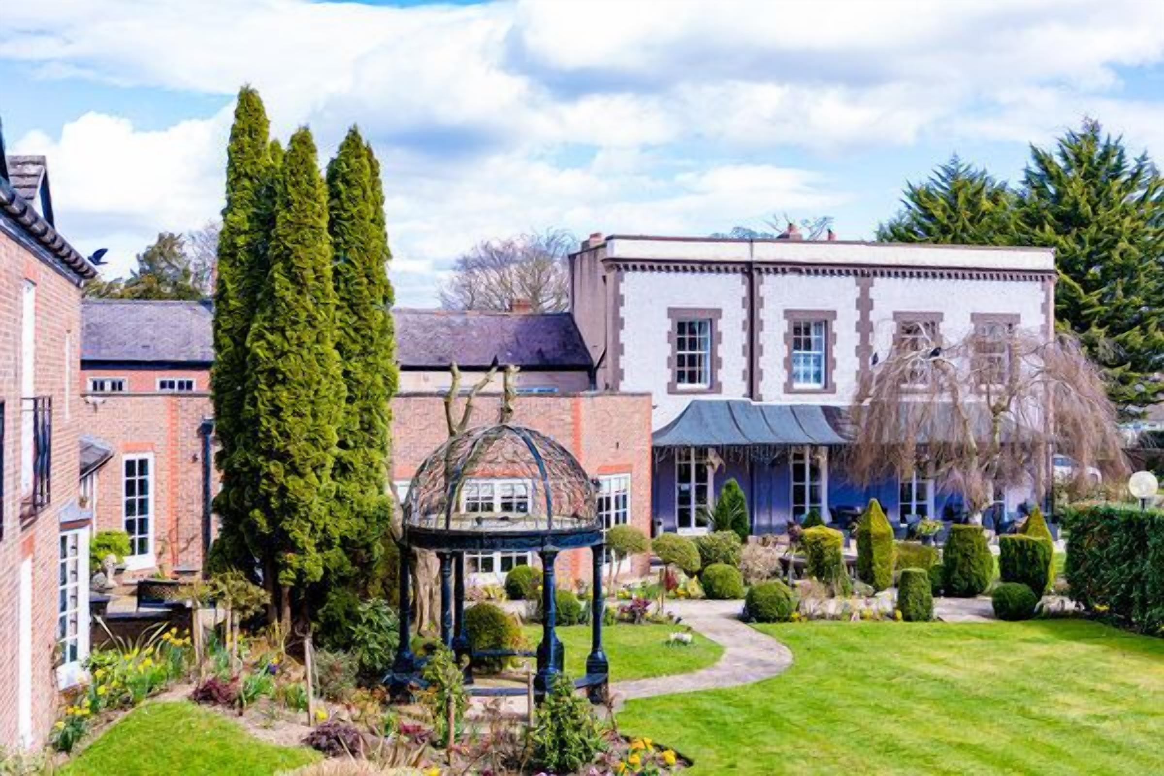 A traditional house with a well-maintained garden, including a gazebo and neatly trimmed hedges.