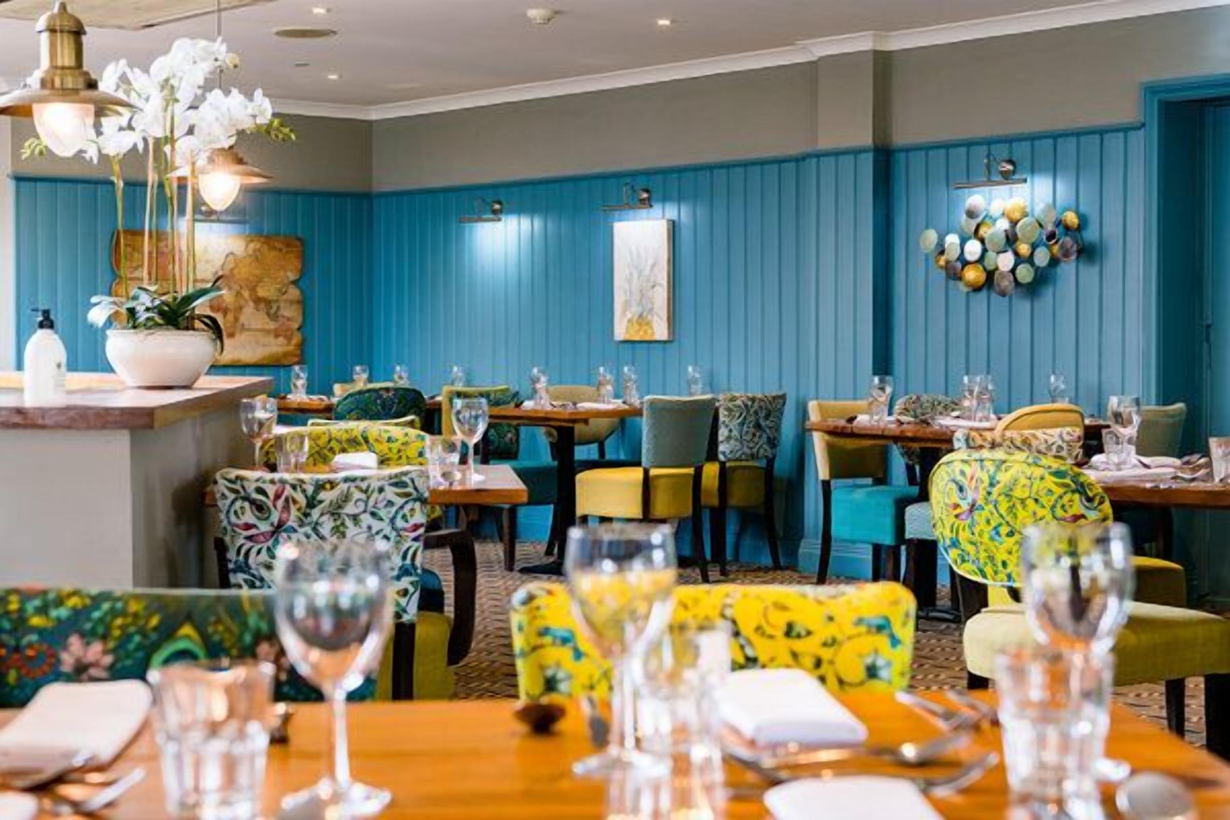 Un restaurant aux murs recouverts de panneaux bleus, aux chaises colorées et offrant une variété de décorations de table.