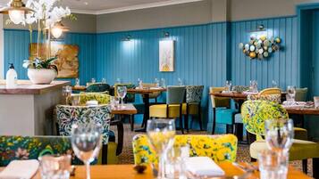 Un restaurant aux murs recouverts de panneaux bleus, aux chaises colorées et offrant une variété de décorations de table.