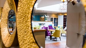 A modern interior with a round mirror reflecting a dining area featuring yellow chairs and a table. - Rossett Hall Hotel (Wrexham)