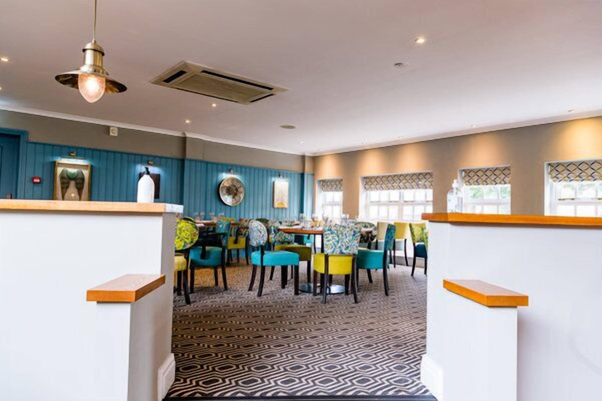 Un restaurante con una decoración azul y blanca, alfombra estampada y sillas de colores.