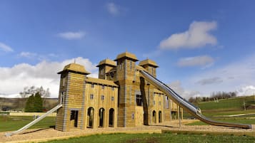 Explore a whimsical castle play structure with towers and a central slide in a lush park setting.