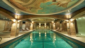 An indoor swimming pool with a mural on the ceiling, lounge chairs, and a stone wall.