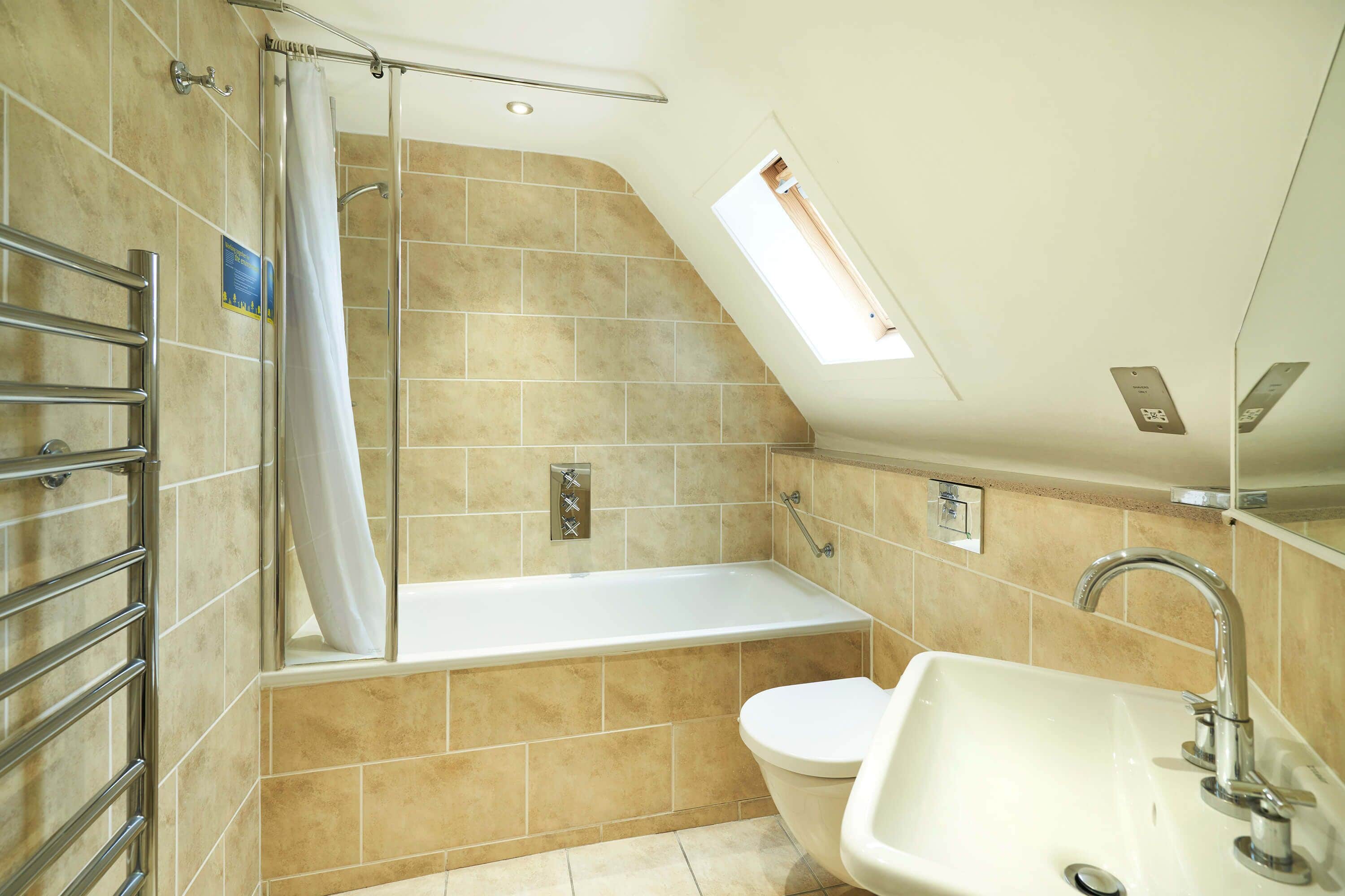 A bathroom with a bathtub, toilet, and sink, featuring a skylight and tiled walls.