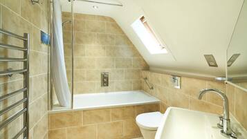 A bathroom with a bathtub, toilet, and sink, featuring a skylight and tiled walls.