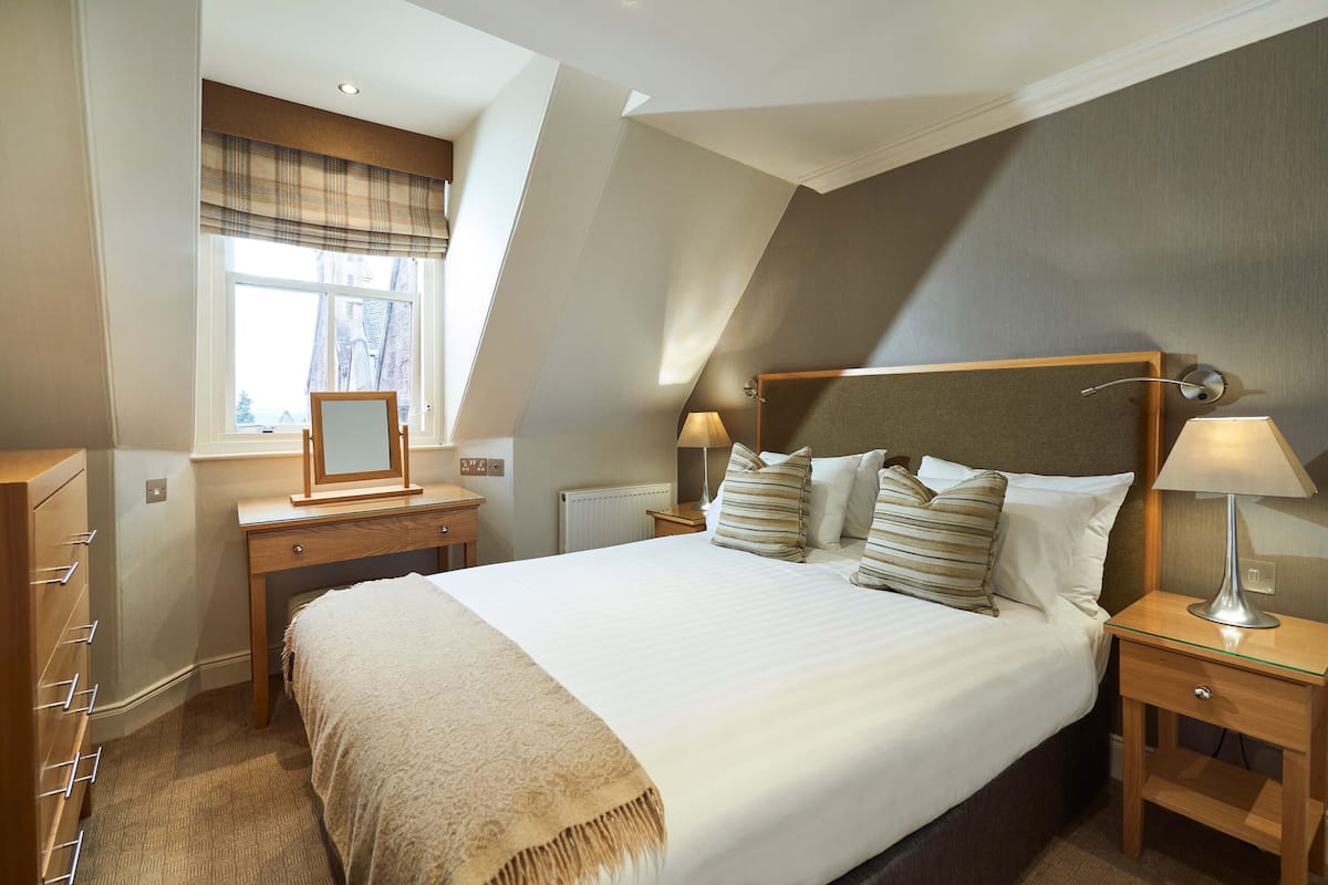 A neatly arranged bedroom with a large bed, bedside tables, a dresser, and a window with a view.
