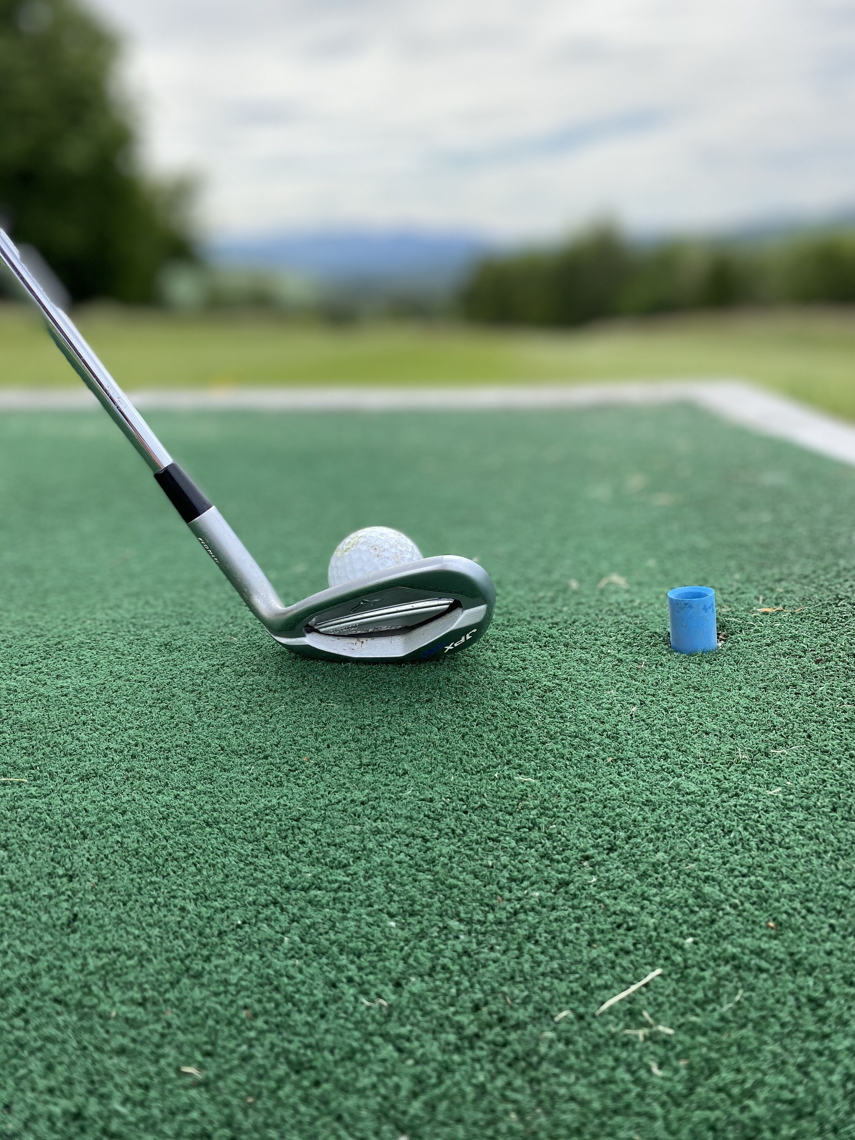 A golf club on a green surface with a golf ball and a blue tee.