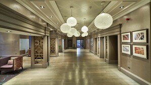 Un vaste couloir d’hôtel doté d’un plancher en bois poli, d’élégants lustres et de tableaux encadrés accrochés aux murs.
