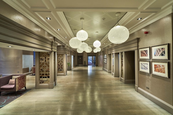 A spacious hotel corridor with a polished wooden floor, elegant chandeliers, and framed pictures on the walls. - Crieff Hydro (Crieff)