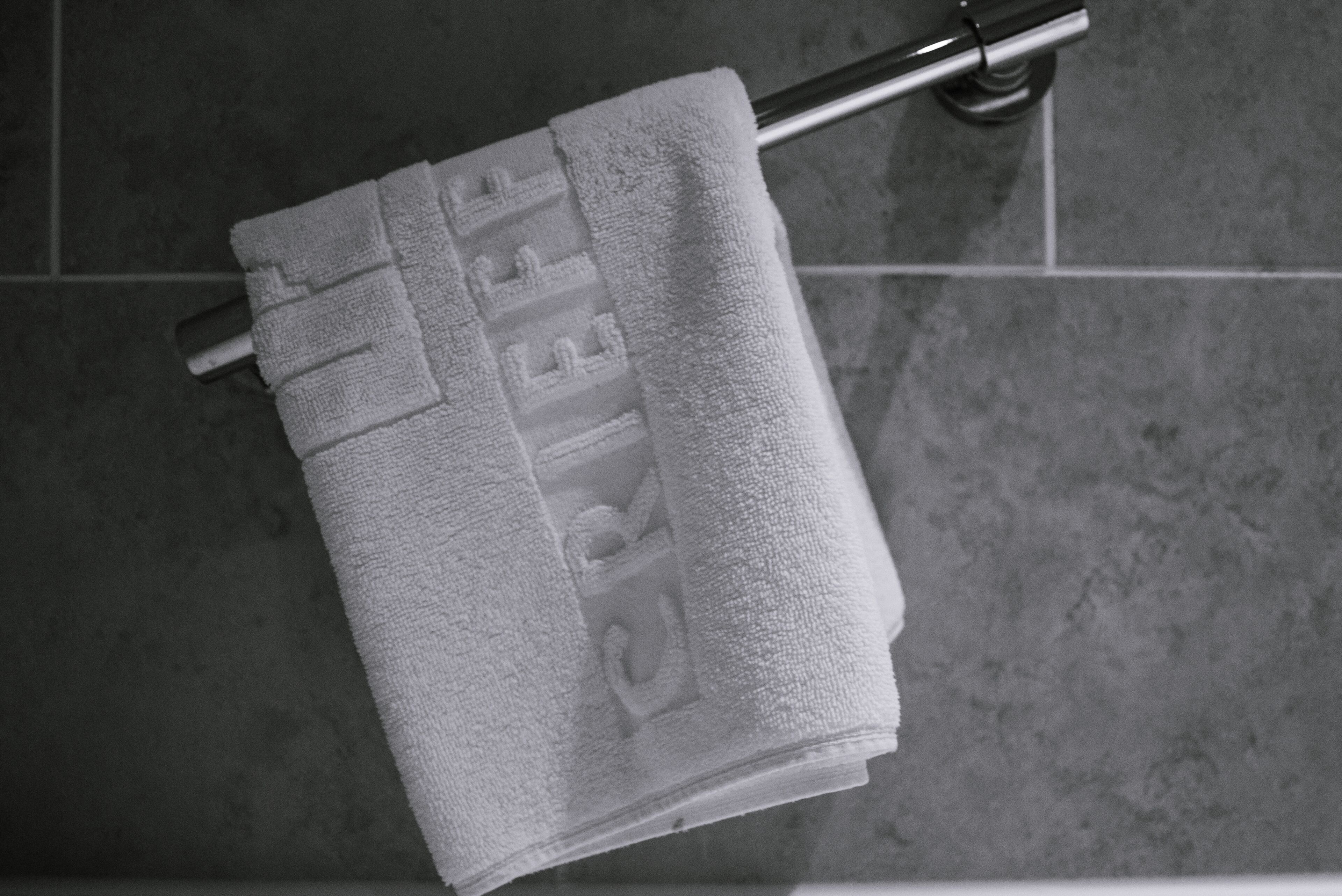 A white towel with embossed text hanging on a metal towel rack in a tiled bathroom.