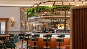 Un espace bar doté de plusieurs tabourets, d’un comptoir avec des bouteilles et de verres suspendus.