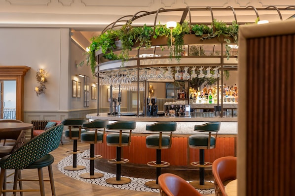 A bar area with multiple stools, a counter with bottles, and hanging glasses. - Crieff Hydro (Crieff)