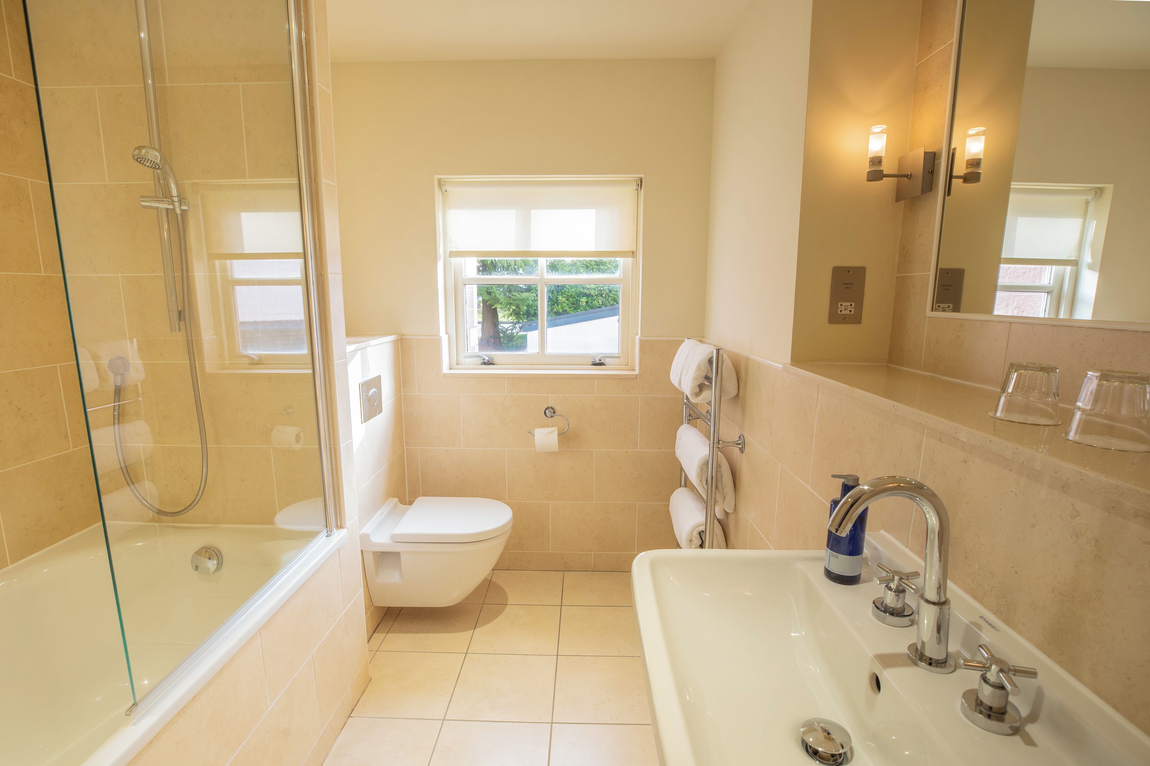 A bathroom with a glass-enclosed shower, a toilet, a sink, and a window.