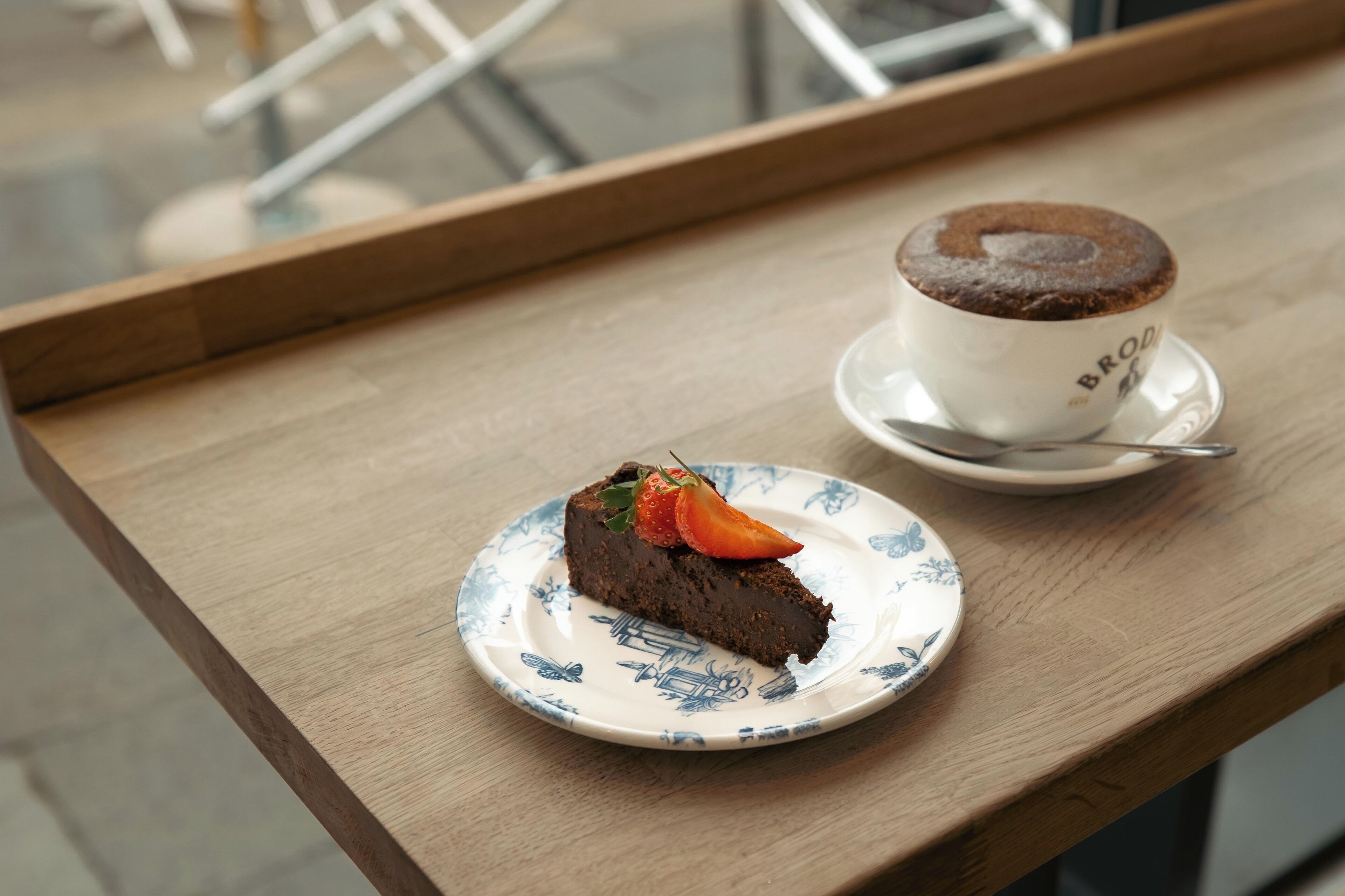 A slice of chocolate cake with a strawberry on a plate, next to a cup of coffee on a wooden table.