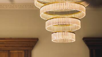 Um lustre de vários níveis com design texturizado, pendurado em um quarto com painéis de madeira e uma obra de arte floral emoldurada na parede.