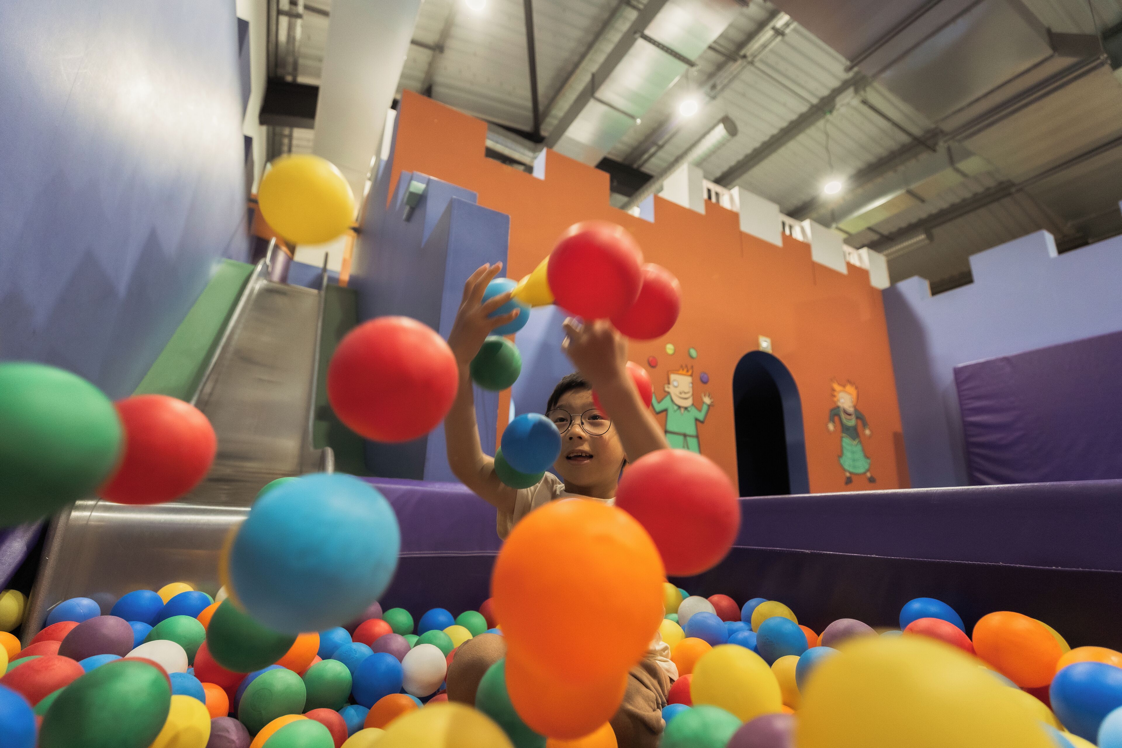 A child playing in a ball pit with colorful balls.