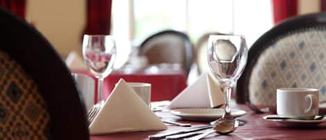 A dining table set with a white napkin, a glass, a cup, and cutlery.