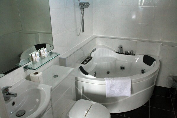A bathroom with a sink, toilet, and a large bathtub with a control panel.