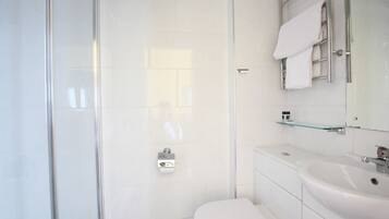 Un baño moderno con cabina de ducha de vidrio, inodoro blanco y lavamanos con repisa de vidrio arriba.