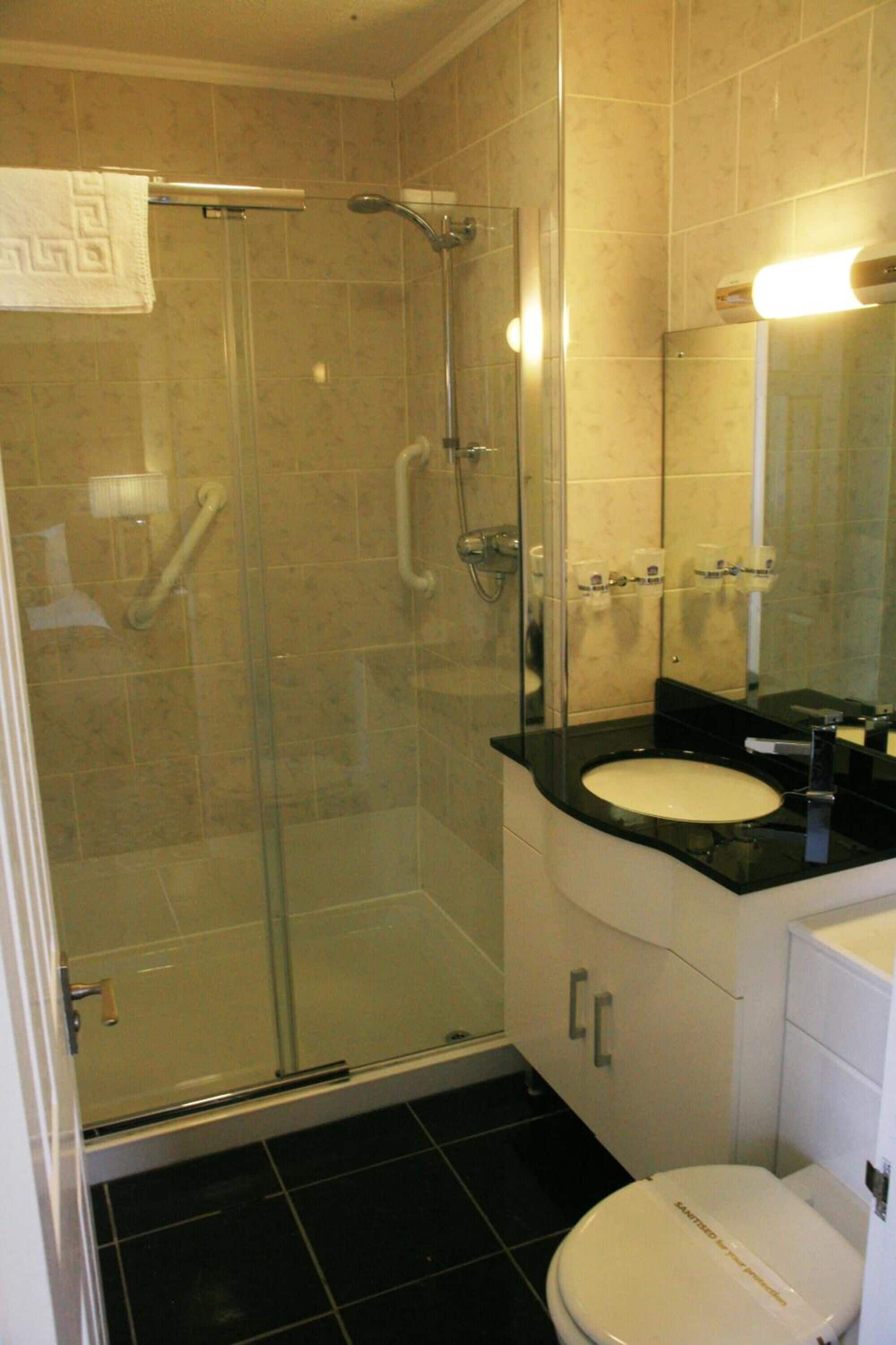 A bathroom with a glass-enclosed shower, a white sink, and a toilet.