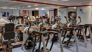 Une salle de sport équipée de plusieurs tapis de course, de miroirs et d’appareils d’exercice.