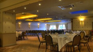 Une salle de banquet avec des tables rondes et des chaises, une moquette à motifs et un éclairage encastré.