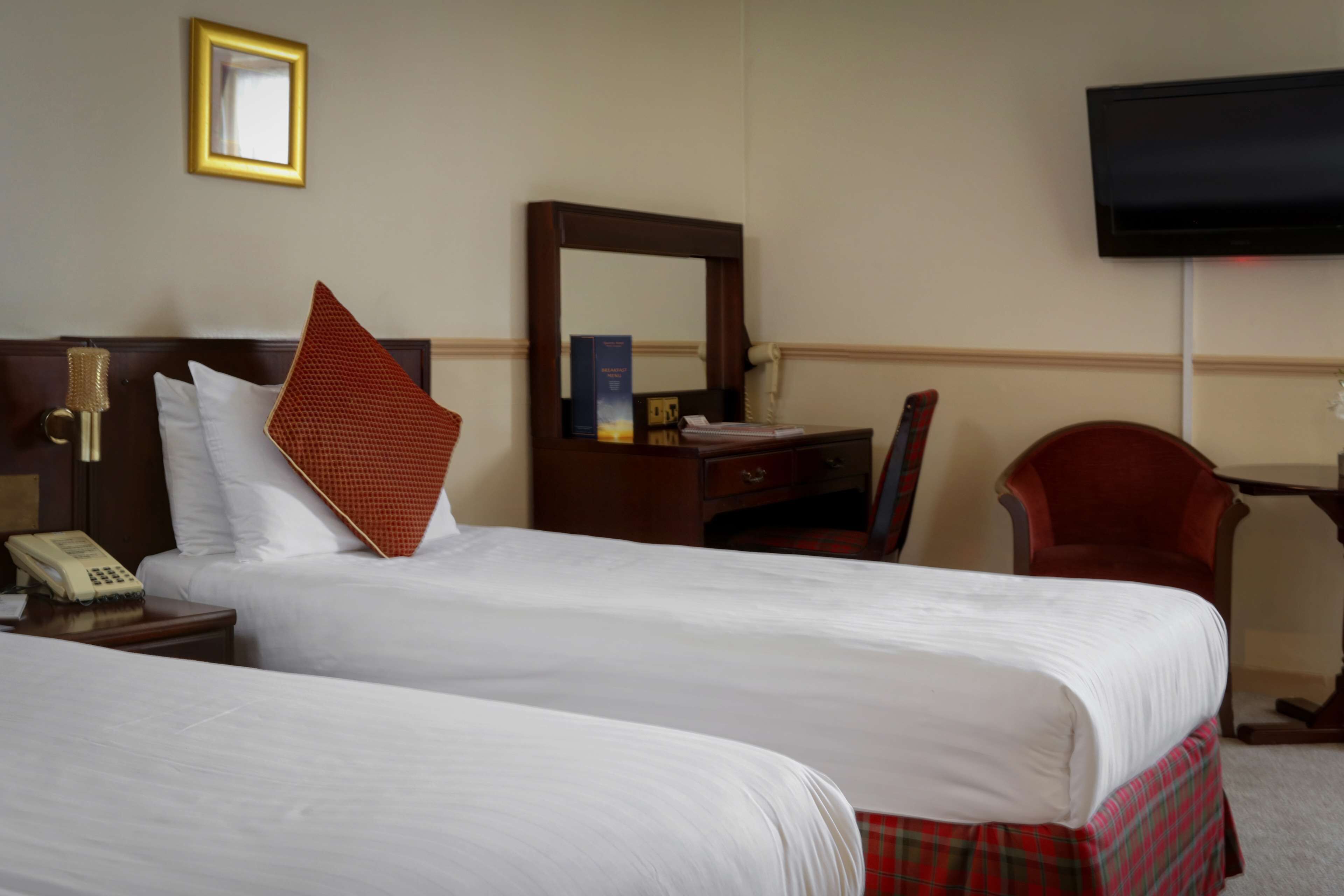 A hotel room with two beds, a desk, a chair, a television, and a telephone.