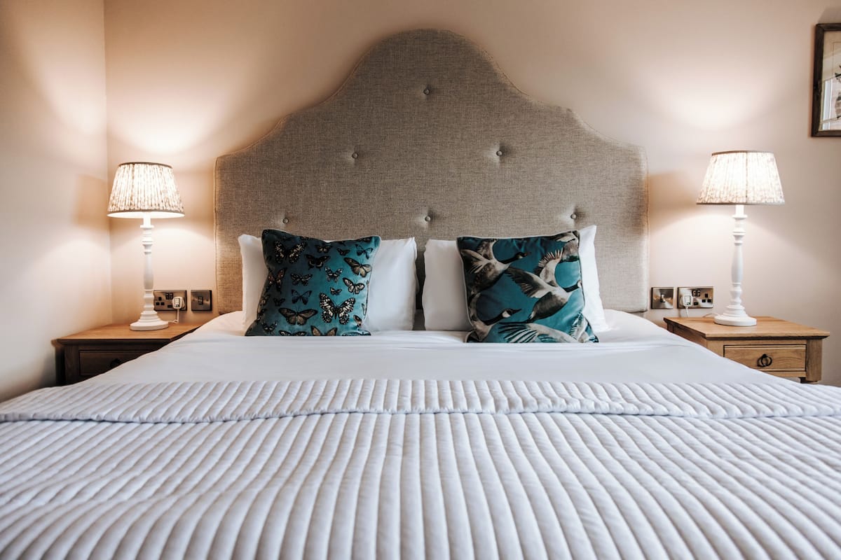 Een net opgemaakt bed met een witte, geribbeld laken, twee nachtkastjes met lampen, en een gestuikt hoofdbord.