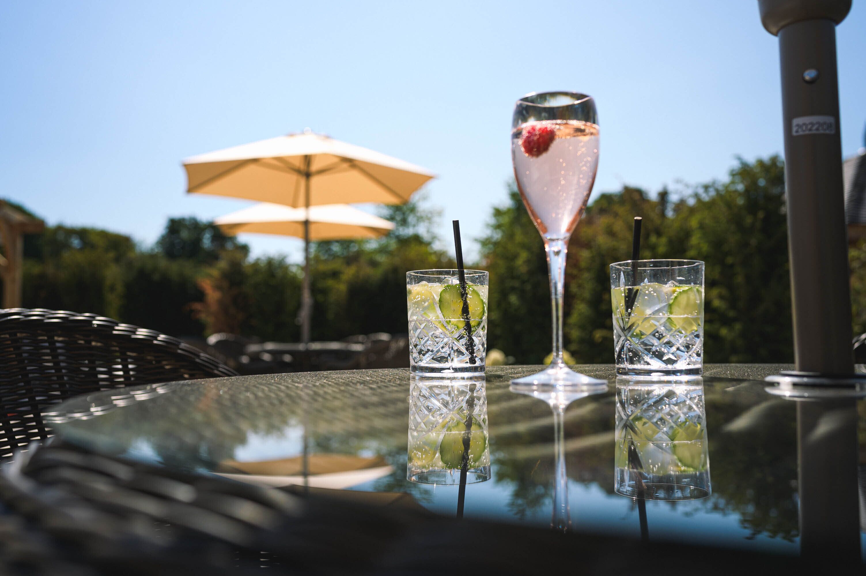 A table with two glasses of a clear beverage with lime and a single glass with a pink drink and a strawberry garnish.