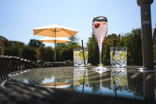 A table with two glasses of a clear beverage with lime and a single glass with a pink drink and a strawberry garnish. - Manor House Hotel & Spa (Stoke-on-Trent)