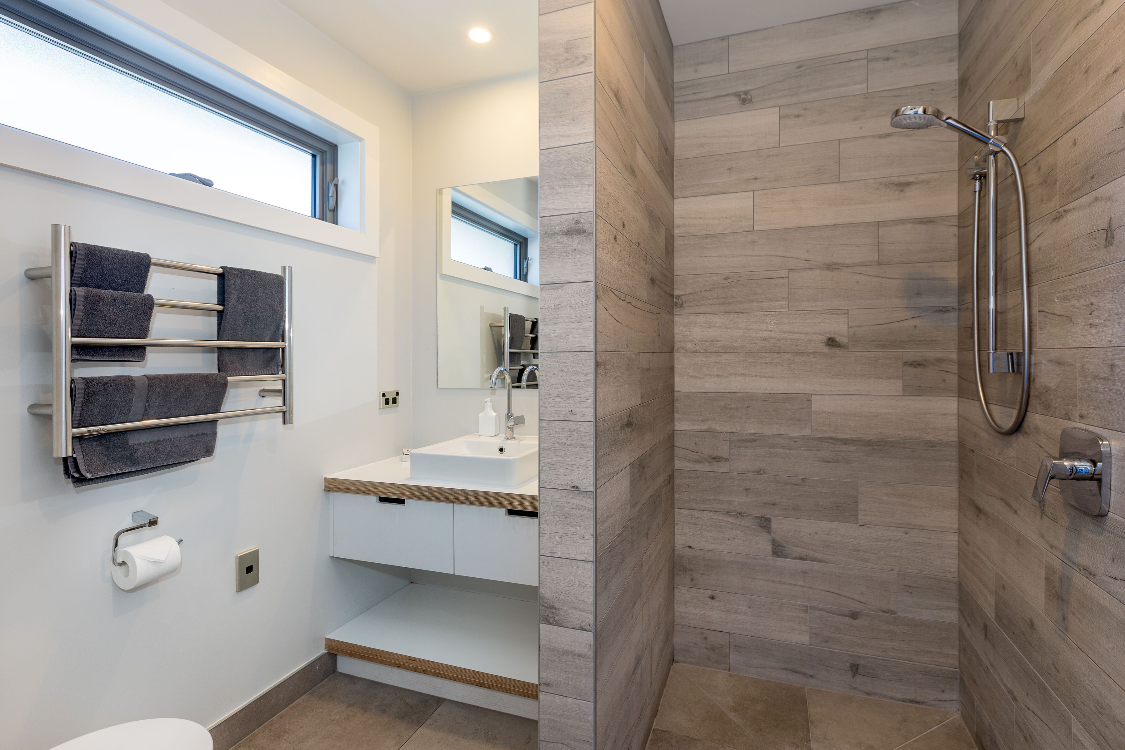 Un baño moderno con piso de madera, un lavamanos blanco, un espejo y una ducha con cabezal de ducha manual.