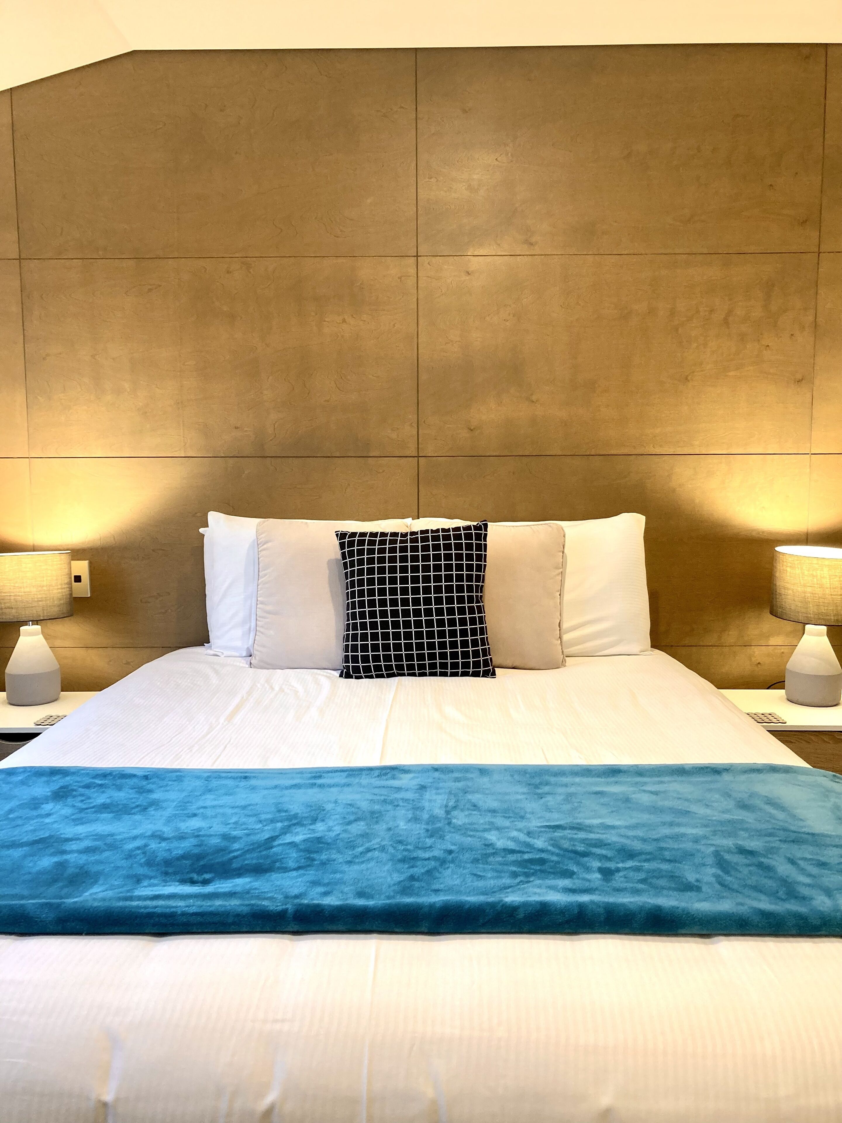 Camera d'albergo con un letto grande, una testiera, due lampade da comodino e una coperta blu.