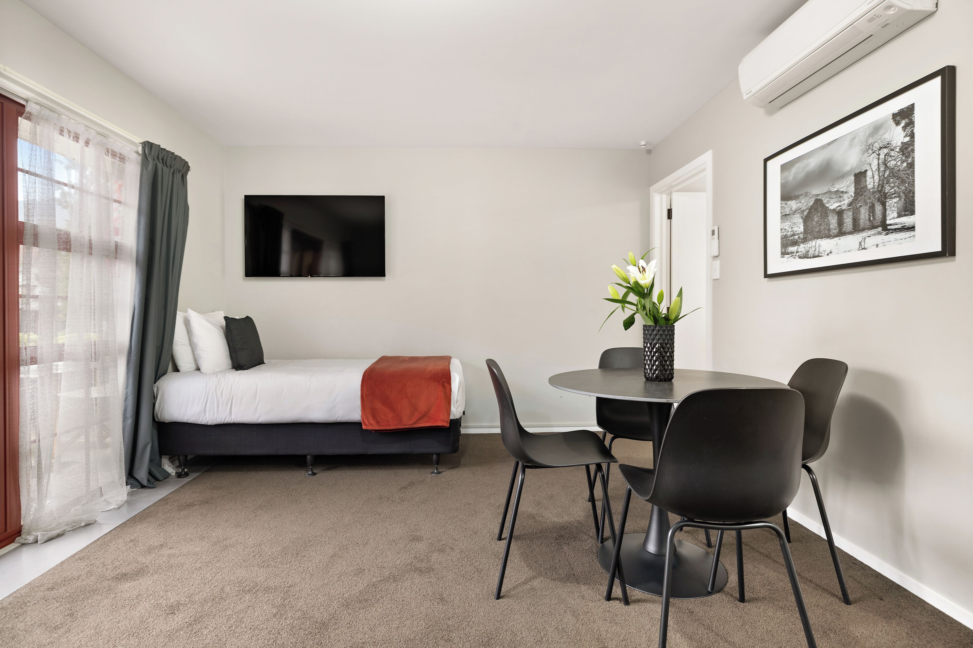 Een moderne hotelkamer met een bed, een eettafel met stoelen, een aan de muur bevestigde televisie en een lijst met een afbeelding.