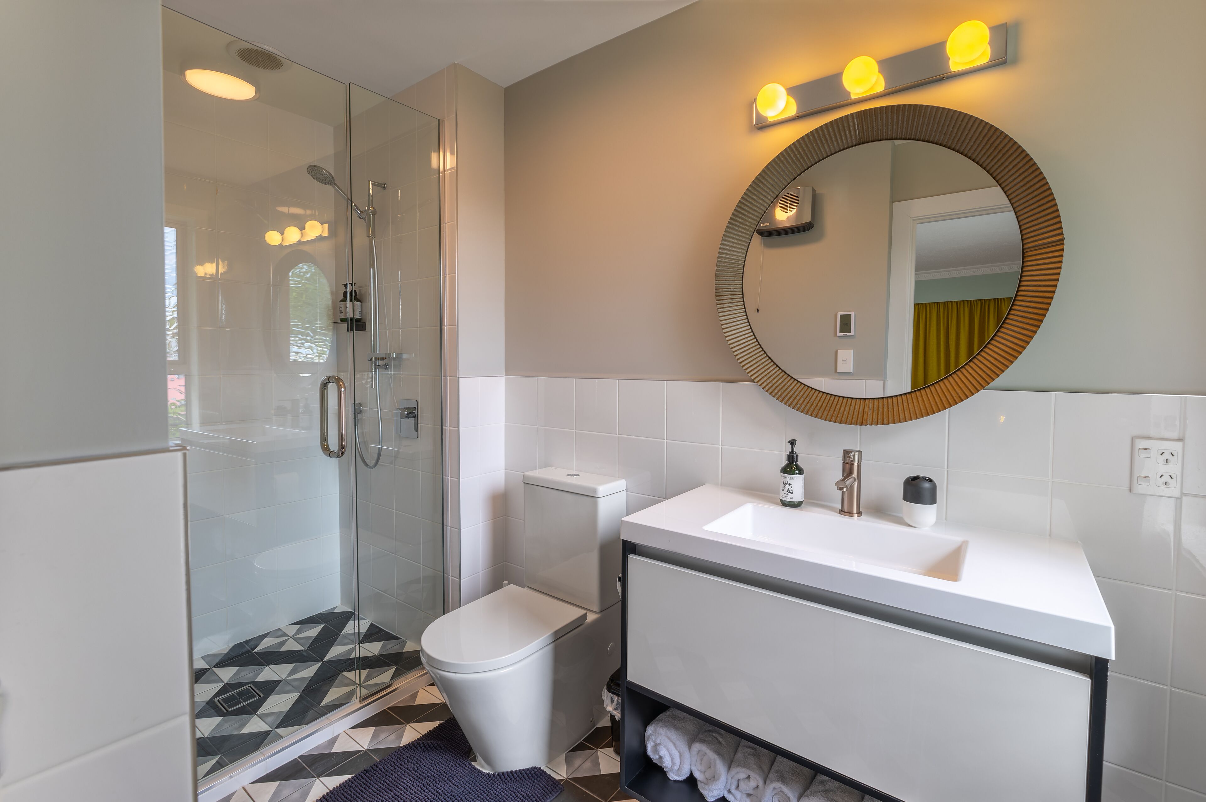 Un baño moderno con ducha envuelta en vidrio, inodoro blanco y tocador con espejo.