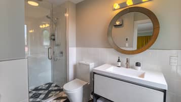 Un baño moderno con ducha envuelta en vidrio, inodoro blanco y tocador con espejo.