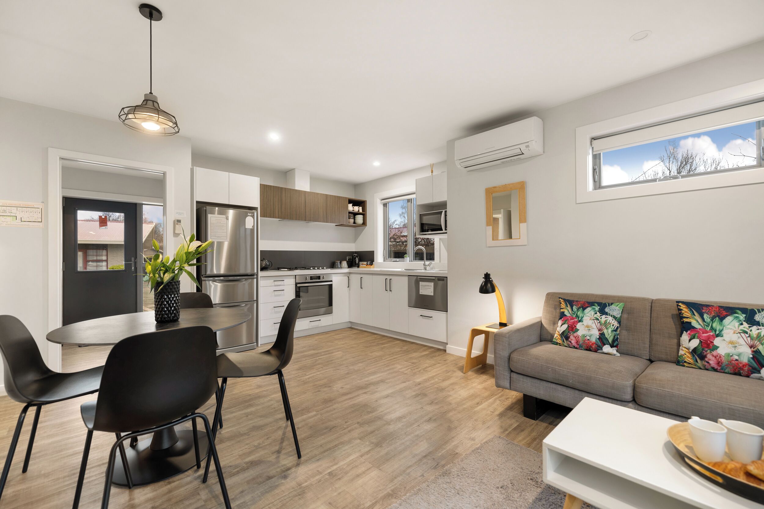 A modern kitchen with white cabinets, a stainless steel refrigerator, and a dining area with a table and chairs.