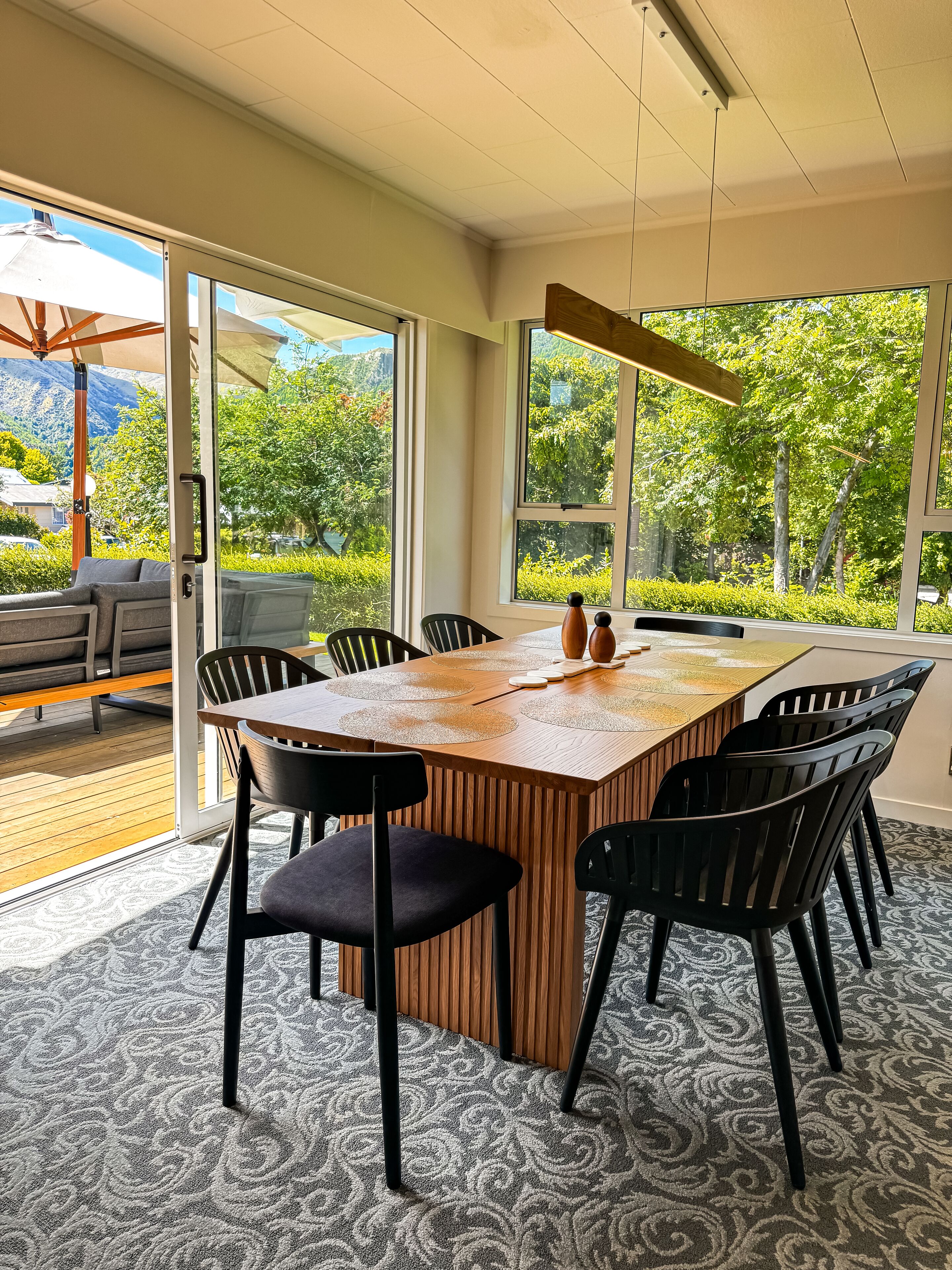 Ein moderner Besprechungsraum mit einem großen Holztisch, schwarzen Stühlen und Blick auf üppiges Grün durch große Fenster.
